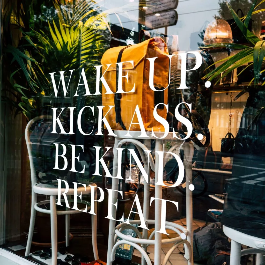 Retail storefront with white window vinyl that says "Wake up. Kick ass. Be kind. Repeat."