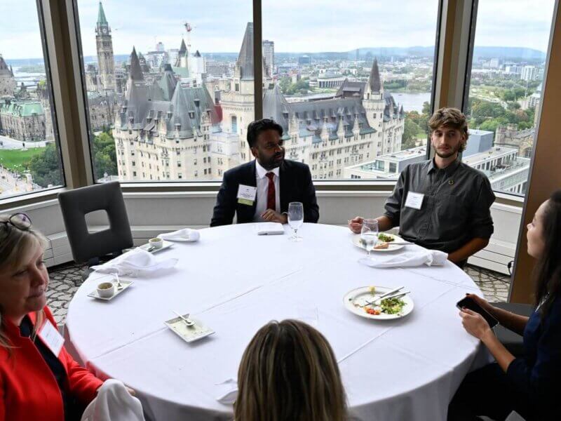 Photo taken during the Together25Ensemble conference featuring several people seated at a round table with white table cloth